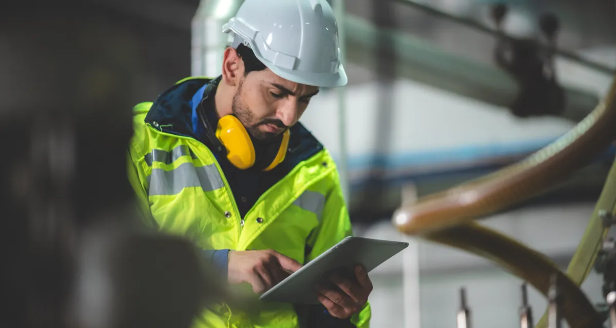 Técnico de capacete e colete refletivo operando tablet em planta industrial
